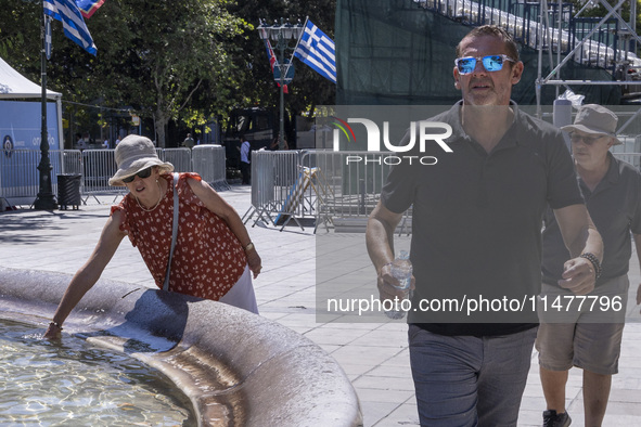 Tourist, visitors and locals are walking past Syntagma Square with the famous fountain during a heatwave in Athens with the high temperature...