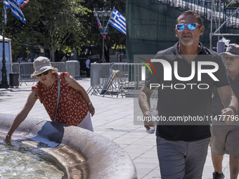 Tourist, visitors and locals are walking past Syntagma Square with the famous fountain during a heatwave in Athens with the high temperature...