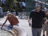 Tourist, visitors and locals are walking past Syntagma Square with the famous fountain during a heatwave in Athens with the high temperature...