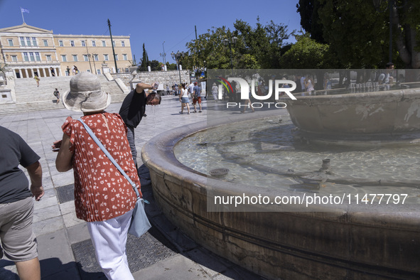 Tourist, visitors and locals are walking past Syntagma Square with the famous fountain during a heatwave in Athens with the high temperature...