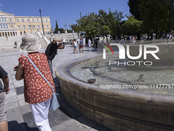 Tourist, visitors and locals are walking past Syntagma Square with the famous fountain during a heatwave in Athens with the high temperature...