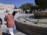 Tourist, visitors and locals are walking past Syntagma Square with the famous fountain during a heatwave in Athens with the high temperature...