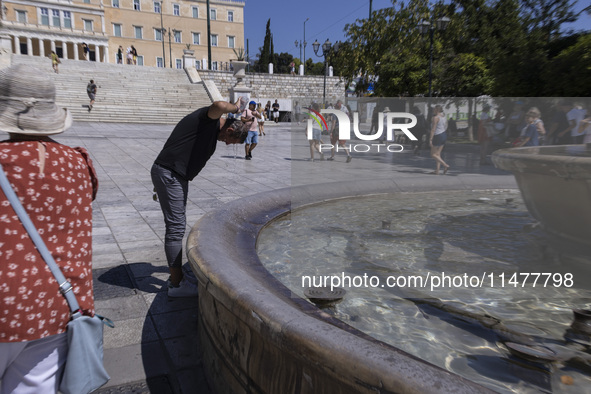 Tourist, visitors and locals are walking past Syntagma Square with the famous fountain during a heatwave in Athens with the high temperature...