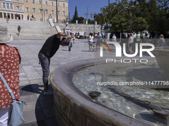 Tourist, visitors and locals are walking past Syntagma Square with the famous fountain during a heatwave in Athens with the high temperature...