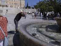 Tourist, visitors and locals are walking past Syntagma Square with the famous fountain during a heatwave in Athens with the high temperature...