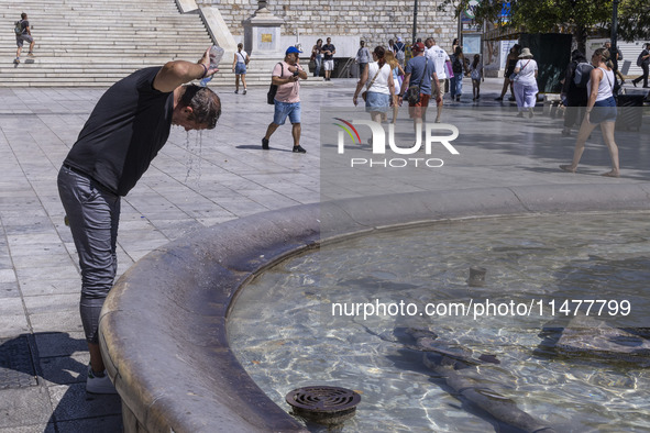 Tourist, visitors and locals are walking past Syntagma Square with the famous fountain during a heatwave in Athens with the high temperature...