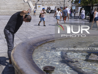 Tourist, visitors and locals are walking past Syntagma Square with the famous fountain during a heatwave in Athens with the high temperature...