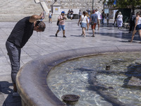 Tourist, visitors and locals are walking past Syntagma Square with the famous fountain during a heatwave in Athens with the high temperature...