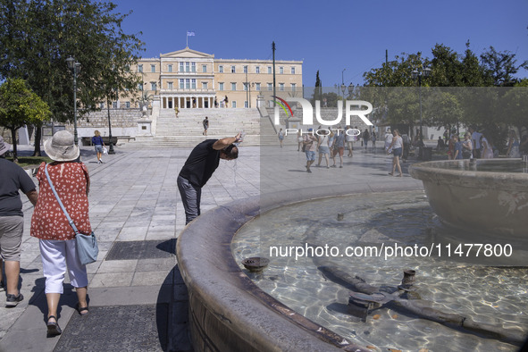 Tourist, visitors and locals are walking past Syntagma Square with the famous fountain during a heatwave in Athens with the high temperature...