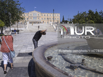 Tourist, visitors and locals are walking past Syntagma Square with the famous fountain during a heatwave in Athens with the high temperature...