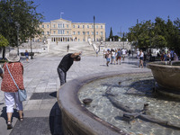 Tourist, visitors and locals are walking past Syntagma Square with the famous fountain during a heatwave in Athens with the high temperature...