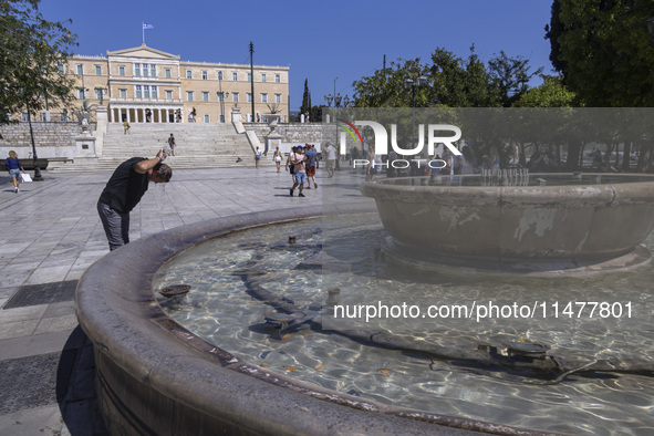 Tourist, visitors and locals are walking past Syntagma Square with the famous fountain during a heatwave in Athens with the high temperature...