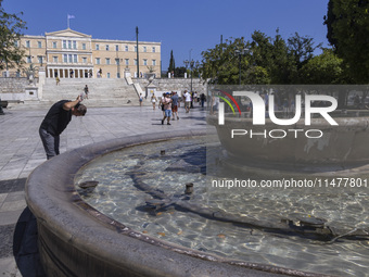 Tourist, visitors and locals are walking past Syntagma Square with the famous fountain during a heatwave in Athens with the high temperature...