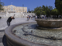 Tourist, visitors and locals are walking past Syntagma Square with the famous fountain during a heatwave in Athens with the high temperature...