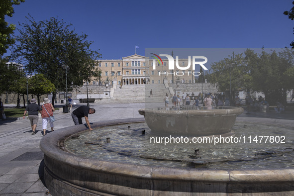 Tourist, visitors and locals are walking past Syntagma Square with the famous fountain during a heatwave in Athens with the high temperature...