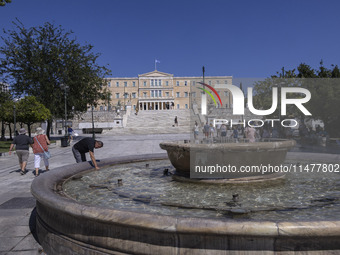 Tourist, visitors and locals are walking past Syntagma Square with the famous fountain during a heatwave in Athens with the high temperature...