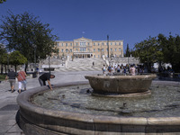 Tourist, visitors and locals are walking past Syntagma Square with the famous fountain during a heatwave in Athens with the high temperature...