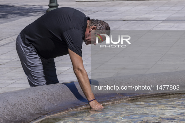 Tourist, visitors and locals are walking past Syntagma Square with the famous fountain during a heatwave in Athens with the high temperature...