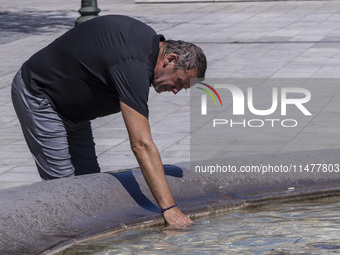 Tourist, visitors and locals are walking past Syntagma Square with the famous fountain during a heatwave in Athens with the high temperature...