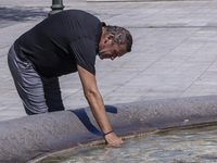 Tourist, visitors and locals are walking past Syntagma Square with the famous fountain during a heatwave in Athens with the high temperature...