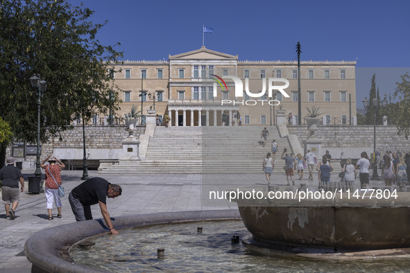 Tourist, visitors and locals are walking past Syntagma Square with the famous fountain during a heatwave in Athens with the high temperature...