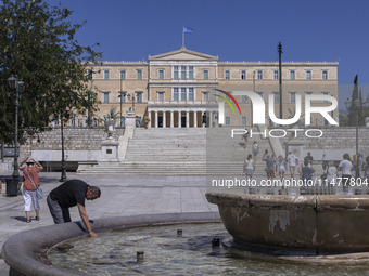 Tourist, visitors and locals are walking past Syntagma Square with the famous fountain during a heatwave in Athens with the high temperature...