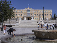 Tourist, visitors and locals are walking past Syntagma Square with the famous fountain during a heatwave in Athens with the high temperature...