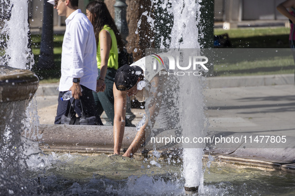 Tourist, visitors and locals are walking past Syntagma Square with the famous fountain during a heatwave in Athens with the high temperature...