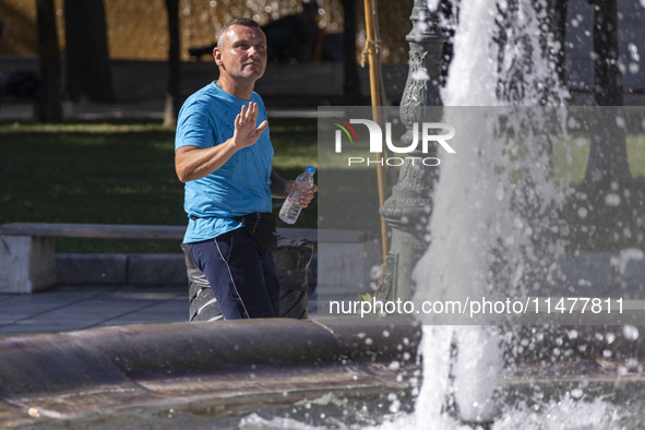 Tourist, visitors and locals are walking past Syntagma Square with the famous fountain during a heatwave in Athens with the high temperature...