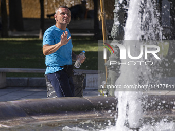 Tourist, visitors and locals are walking past Syntagma Square with the famous fountain during a heatwave in Athens with the high temperature...