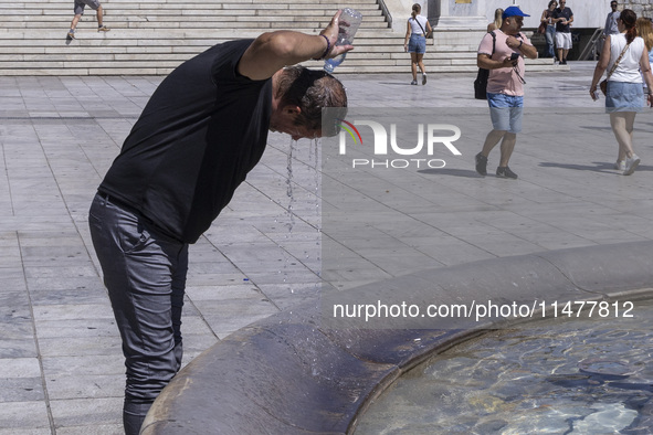 Tourist, visitors and locals are walking past Syntagma Square with the famous fountain during a heatwave in Athens with the high temperature...