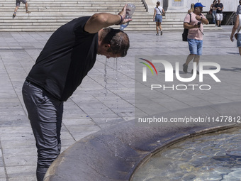 Tourist, visitors and locals are walking past Syntagma Square with the famous fountain during a heatwave in Athens with the high temperature...