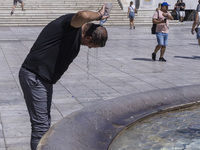 Tourist, visitors and locals are walking past Syntagma Square with the famous fountain during a heatwave in Athens with the high temperature...