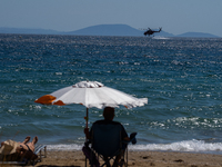 A swimmer is enjoying the sea while a firefighting helicopter is collecting water from it in Nea Makri, Greece, on August 14, 2024, as it is...