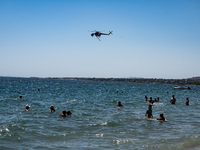 Swimmers are enjoying the sea while a firefighting helicopter is collecting water from it in Nea Makri, Greece, on August 14, 2024, as it is...