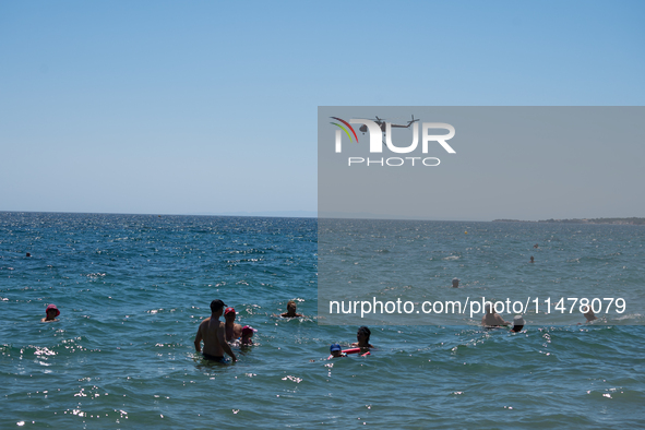 Swimmers are enjoying the sea while a firefighting helicopter is collecting water from it in Nea Makri, Greece, on August 14, 2024, as it is...