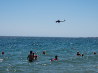 Swimmers are enjoying the sea while a firefighting helicopter is collecting water from it in Nea Makri, Greece, on August 14, 2024, as it is...