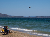 Swimmers are enjoying the sea while a firefighting helicopter is collecting water from it in Nea Makri, Greece, on August 14, 2024, as it is...