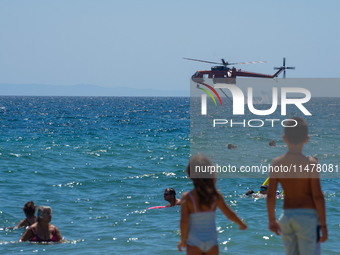 Two children are in the sea, watching the firefighting helicopter collect water from the sea in Nea Makri, Greece, on August 14, 2024, as it...