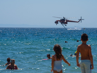 Two children are in the sea, watching the firefighting helicopter collect water from the sea in Nea Makri, Greece, on August 14, 2024, as it...