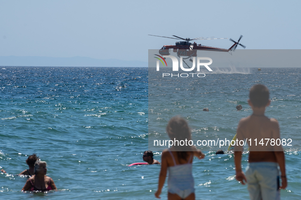 Two children are in the sea, watching the firefighting helicopter collect water from the sea in Nea Makri, Greece, on August 14, 2024, as it...