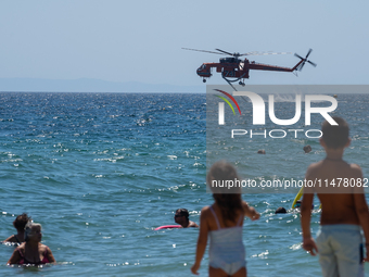 Two children are in the sea, watching the firefighting helicopter collect water from the sea in Nea Makri, Greece, on August 14, 2024, as it...