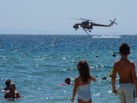 Two children are in the sea, watching the firefighting helicopter collect water from the sea in Nea Makri, Greece, on August 14, 2024, as it...