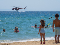 Two children are in the sea, watching the firefighting helicopter collect water from the sea in Nea Makri, Greece, on August 14, 2024, as it...