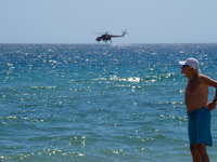 A swimmer is enjoying the sea while a firefighting helicopter is collecting water from it in Nea Makri, Greece, on August 14, 2024, as it is...