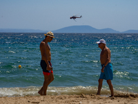 Bathers are enjoying the sea while a firefighting helicopter is collecting water from it in Nea Makri, Greece, on August 14, 2024, as it is...