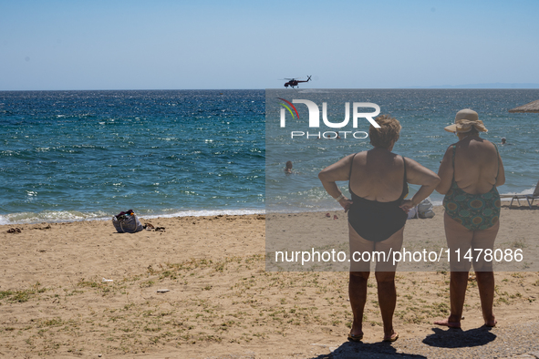 Bathers are enjoying the sea while a firefighting helicopter is collecting water from it in Nea Makri, Greece, on August 14, 2024, as it is...