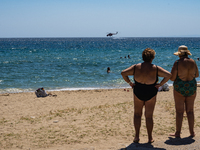 Bathers are enjoying the sea while a firefighting helicopter is collecting water from it in Nea Makri, Greece, on August 14, 2024, as it is...