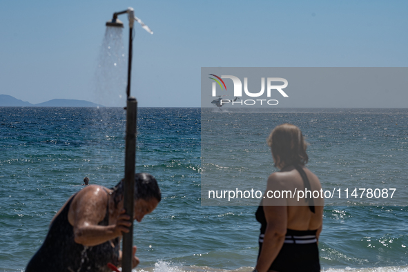 Bathers are enjoying the sea while a firefighting helicopter is collecting water from it in Nea Makri, Greece, on August 14, 2024, as it is...