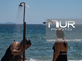 Bathers are enjoying the sea while a firefighting helicopter is collecting water from it in Nea Makri, Greece, on August 14, 2024, as it is...